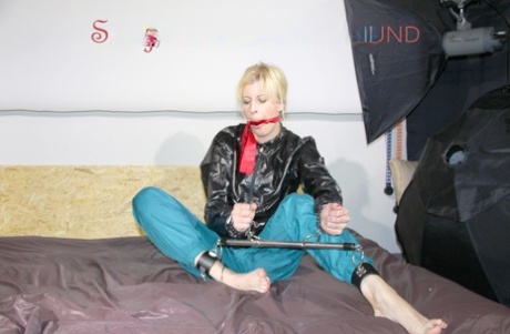 Barefoot blonde sports a gag while attached to a spreader bar in nylon attire 37632411